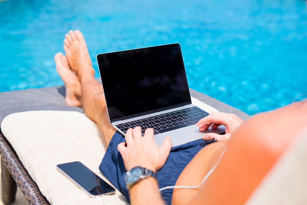 Homme en train de surfer sur le web au bord de sa piscine.
