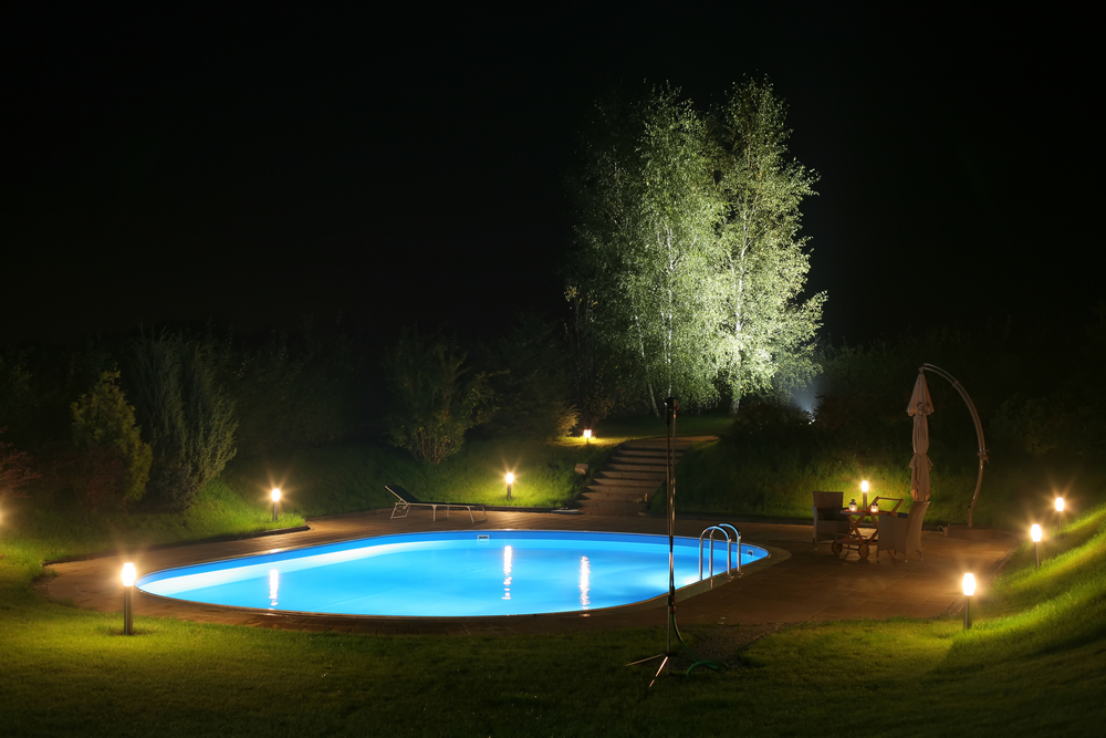 Piscine de nuit, éclairée par des lumières dans le jardin.